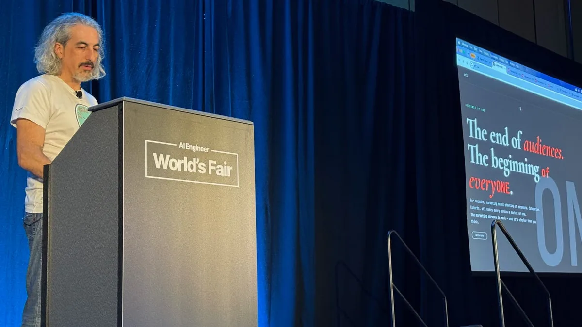 Speaker behind an AI Engineer World’s Fair lectern, with blue curtains and a projected webpage about audiences to his right.