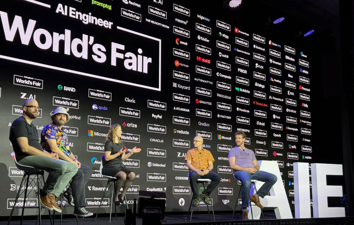 Five people sit on tall stools before an AI Engineer World’s Fair sponsor backdrop; the central participant gestures while holding a microphone.